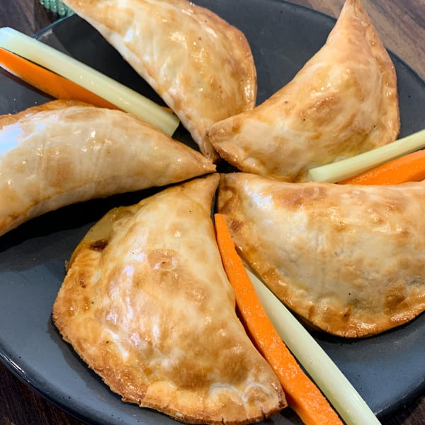Five golden-brown empanadas arranged on a dark plate with carrot and celery sticks.