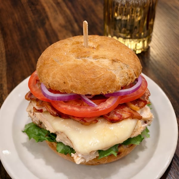 PREN's chicken sandwich with melted cheese, bacon, tomato, onion, and lettuce on a bun.