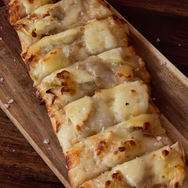 PREN's cheesy flatbread, cut into strips, with melted cheese and flaky salt on a wooden board.