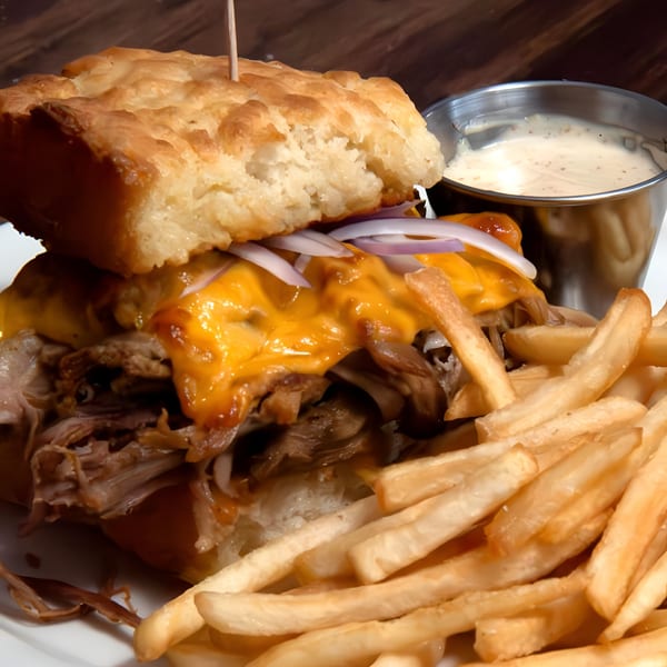 PREN's pulled pork sandwich with melted cheese, red onions, and a side of fries and dipping sauce.